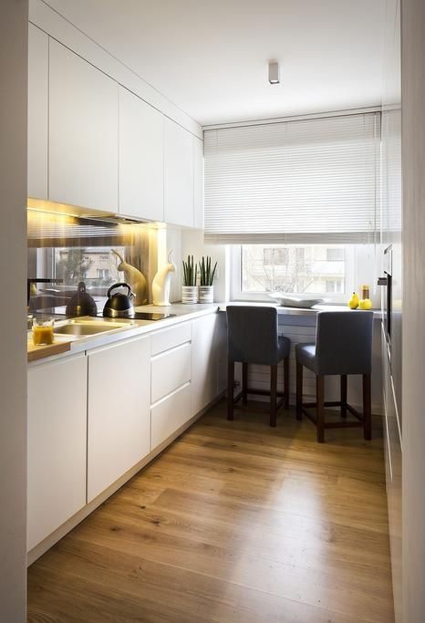 a white, minimalist kitchen with a glossy backsplash, built-in lights and a windowsill breakfast bar
