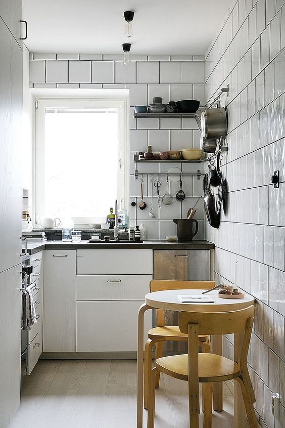A white modern kitchen, fully lined with tiles, black countertops, a round table and stools, is comfortable