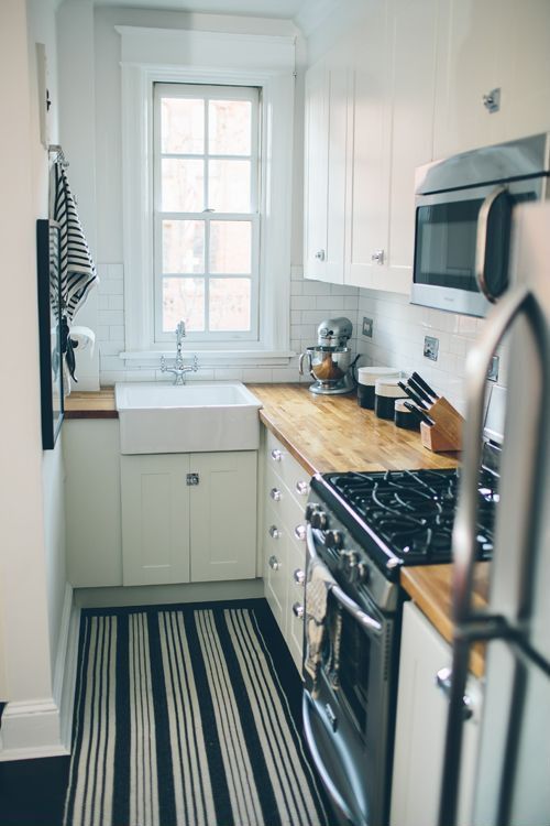 a white modern kitchen with butcher block countertops, a white tile backsplash, a striped rug and neutral handles