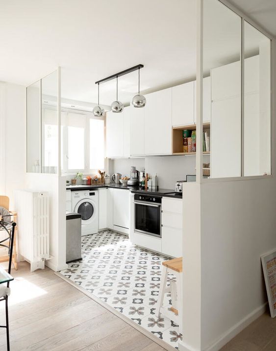 a white, elegant kitchen with a white splashback, black worktops and metal lamps and a printed tile floor