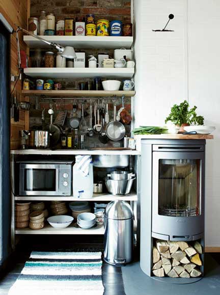 a tiny kitchen corner with open shelves, a small hotplate, a microwave and a wood-burning stove next to it that also served as a countertop
