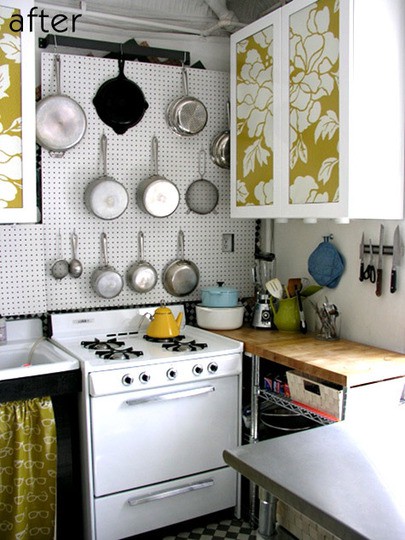 a small, modern kitchen with floral-patterned cabinets, a pegboard for storing pans, a stove, and butcher block countertops