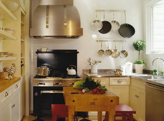 a rustic kitchen in warm colors with metal worktops, built-in cupboards and shelves, a large extractor hood and a small table with red stools