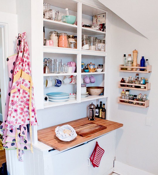 a tiny white kitchen with an open cabinet with shelves, a butcher block countertop and some shelves for storage on the wall