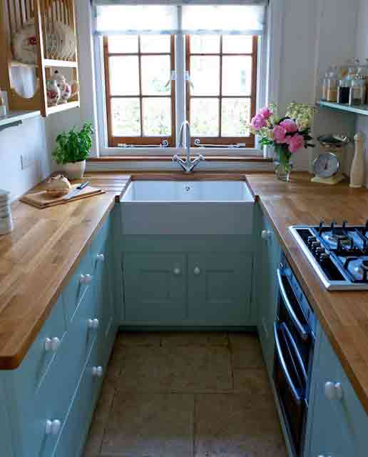A tiny blue kitchen with butcher block countertops and open shelving above the cabinets and views is cozy and cool
