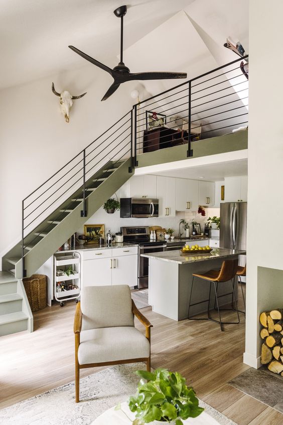 a memorable space with an olive green staircase, cabinets and a gray kitchen island, stone countertops and built-in lights