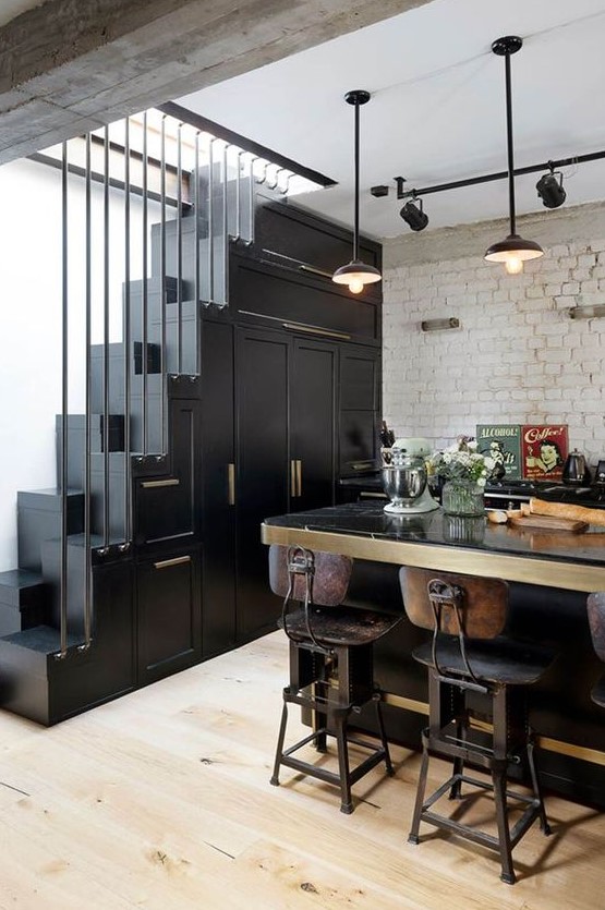 A striking vintage black kitchen with cupboards built into the stairs, a large table that serves as a kitchen island and vintage decor