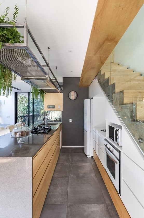 a modern white kitchen with elegant built-in cupboards in the stairwell, a large kitchen island and a metal shelf with green plants