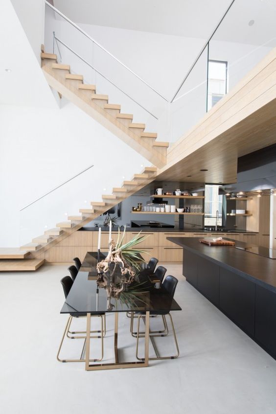A large stained kitchen built in below the stairs with a mirrored backsplash and open shelving, a black kitchen island
