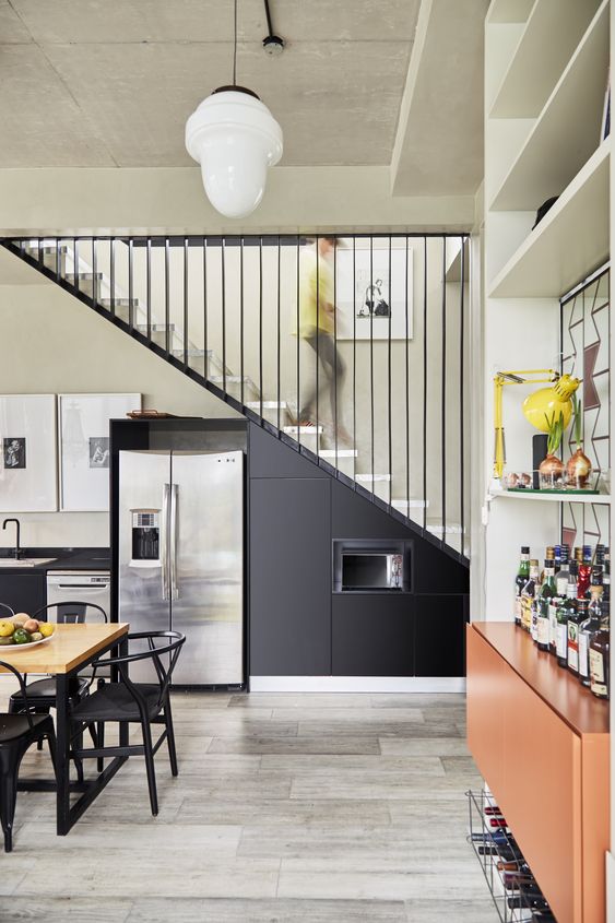 A modern black kitchen with metal cabinets integrated under the stairs, built-in appliances and black chairs is a cool idea