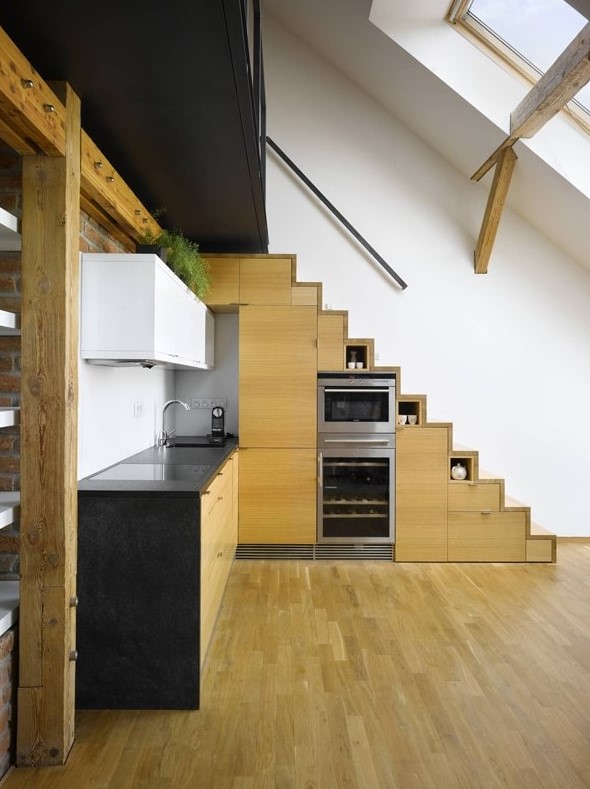 a modern contrasting kitchen with a stained wood staircase that includes cupboards, more wooden cupboards and white and black worktops