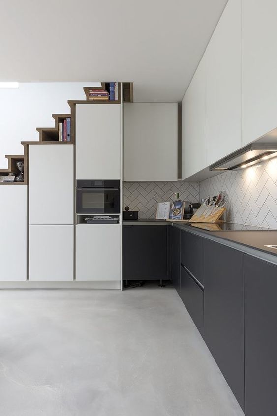 A modern kitchen in graphite gray and white with sleek cabinets, a herringbone tile backsplash and built-in lights