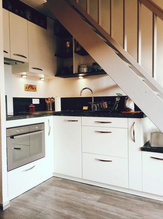 A modern kitchen, partially placed under the stairs, with built-in lighting and black worktops, is a clever and cool idea