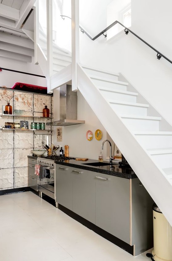 A modern kitchen under the stairs with gray lower row of cabinets, open shelves on the wall and bright decor