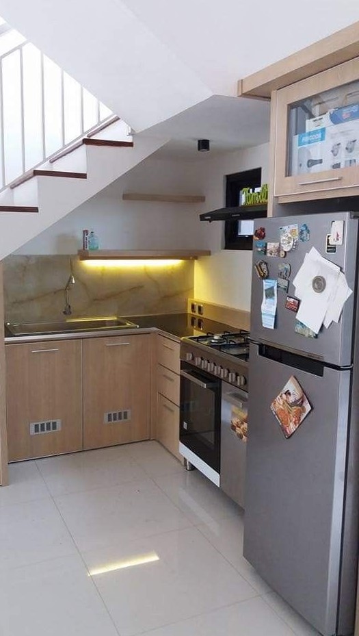 a modern kitchen with lower wooden cabinets under the stairs, open shelving with lights and some appliances