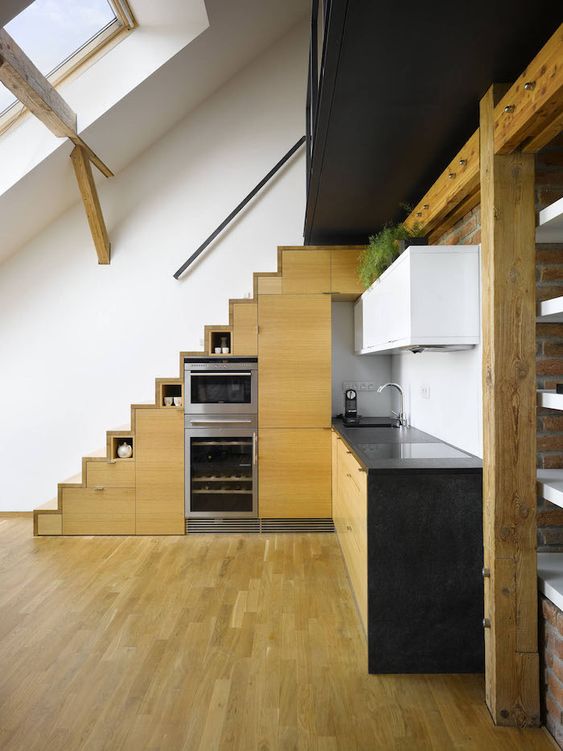 a modern kitchen with stained cabinets built into the stairs, black countertops, white upper cabinets and green plants