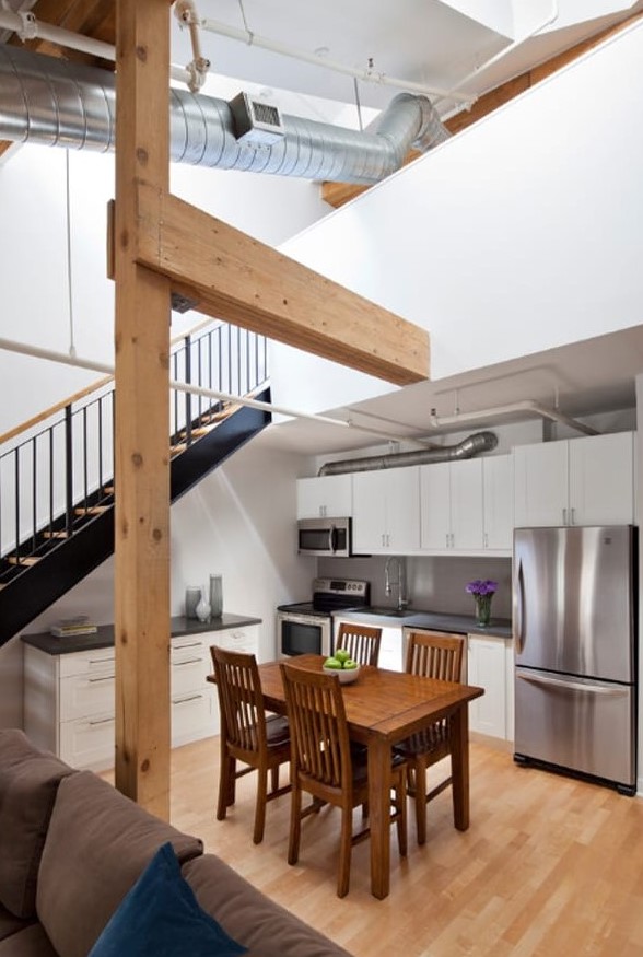 a modern kitchen with white cabinets and black countertops under the stairs and a stained wood dining set