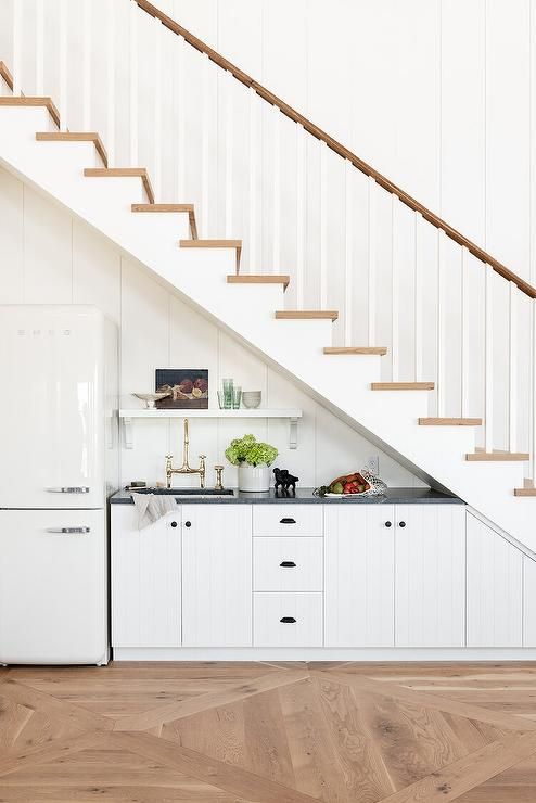 A pretty under-stairs farmhouse kitchen with planked booths, black countertops, a refrigerator, and shelving is cool