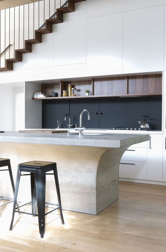 a sophisticated, modern kitchen with sleek built-in cabinets under the stairs, a black splashback and an eye-catching island