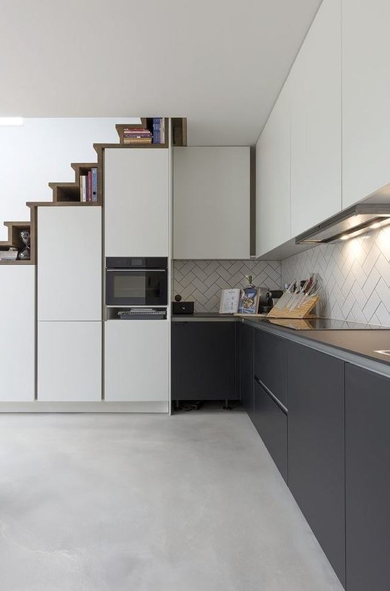 a sleek, modern kitchen with upper white and lower soot cabinets, a herringbone backsplash and a staircase that hides storage compartments
