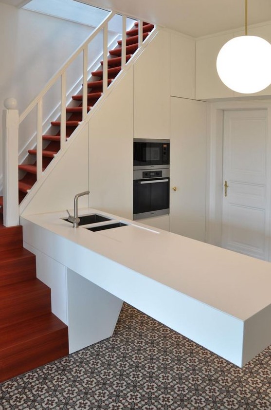 an elegant white kitchen, partially integrated into the stairwell, with an architectural kitchen island and a pendant lamp