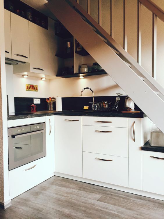 A small under-stairs kitchen with white cabinets, black countertops, and built-in lights is a beautiful space