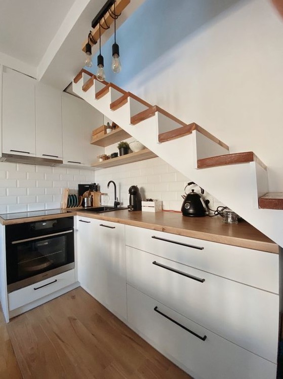 a small Scandinavian kitchen under the stairs, with butcher block countertops and a white brick backsplash, and hanging lamps