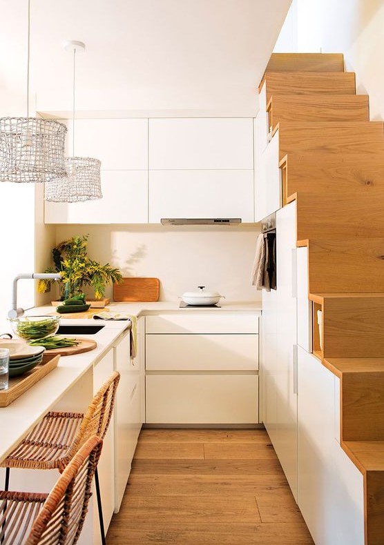 a small modern white kitchen, partially integrated into the stairwell, with a kitchen island that doubles as a dining area
