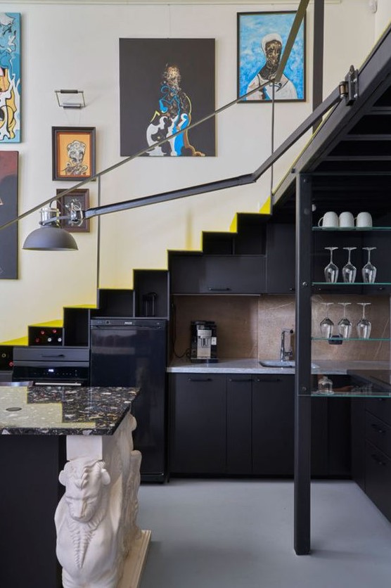a staircase with an integrated black kitchen, open glass shelves, a kitchen island, some decor and a black wall light