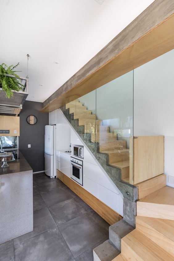 a stylish modern kitchen with sleek white cabinets built under the stairs, a concrete kitchen island and lots of greenery