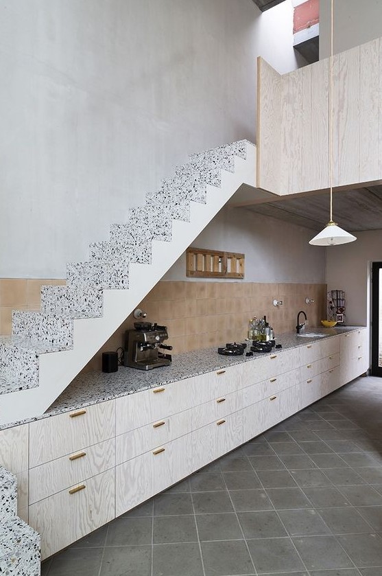 a stylish modern kitchen with whitewashed base cabinets under the stairs, a tiled splashback and terrazzo worktops