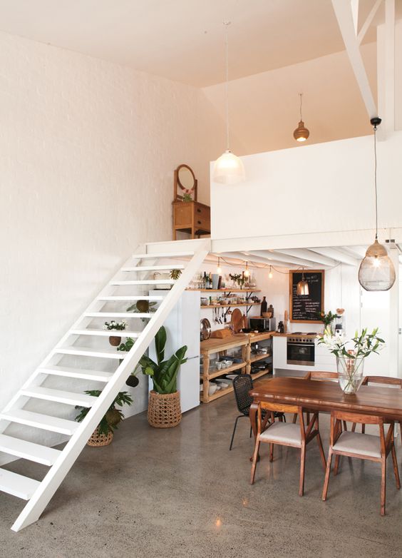 A stylish, modern loft with an under-stairs kitchen, open plan storage units and potted plants, and an adjacent dining area
