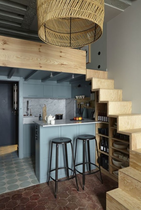 a small but chic kitchen with a staircase that serves to store things, gray cabinets and a kitchen island that also serves as a dining area
