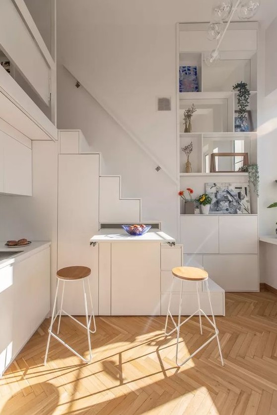 A tiny white kitchen, partially integrated into the stairwell and featuring an extendable table, is a clever solution if you're short on space