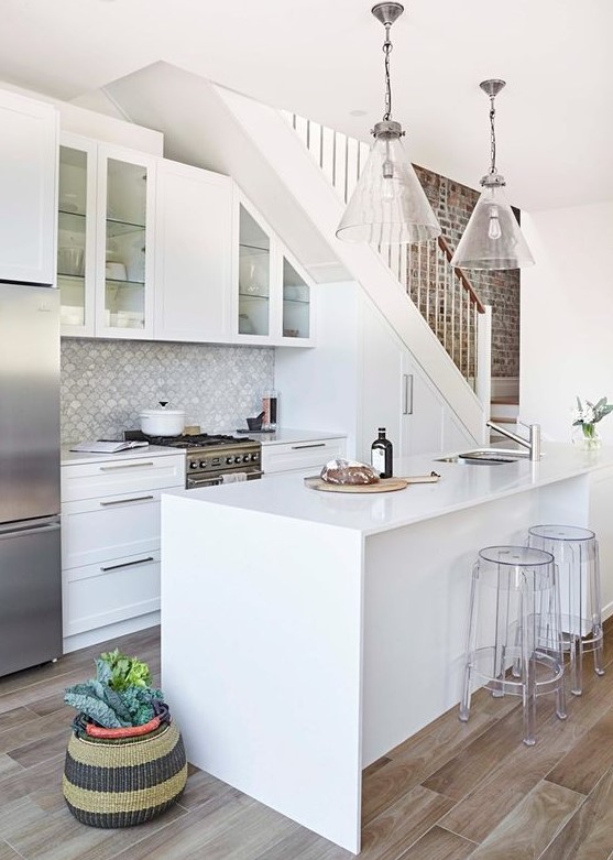 A white modern farmhouse kitchen under the stairs with built-in cabinets, a shell tile backsplash and a kitchen island
