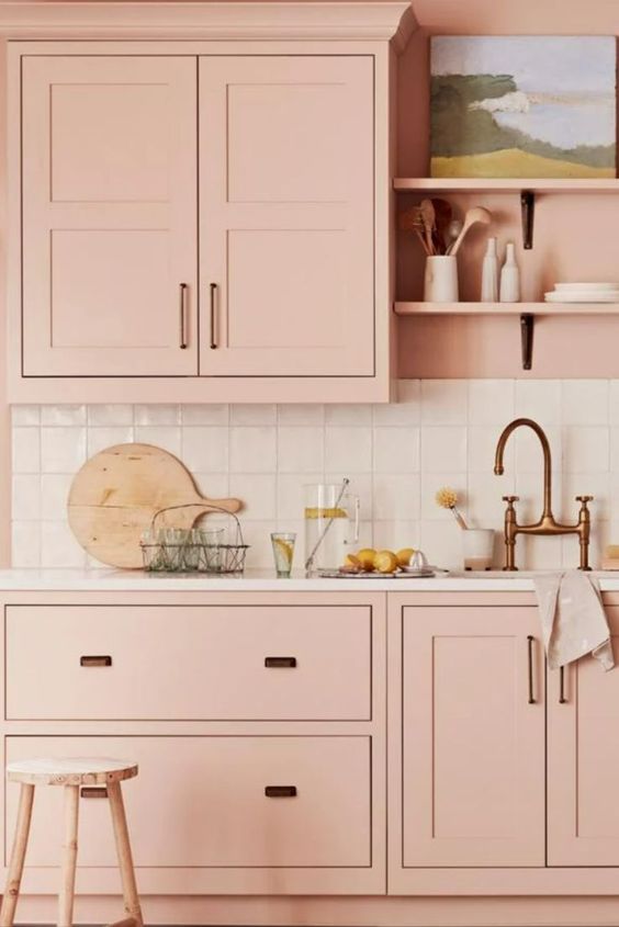 a blush kitchen with a white square tile backsplash and white countertops, black handles and a brass faucet