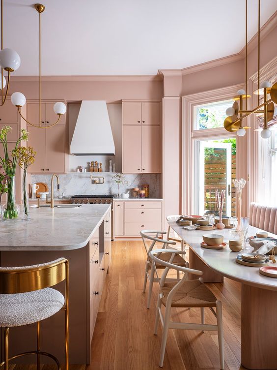 a blush kitchen with elegant cabinets, a large dining area with a sofa, an oval table, a large kitchen island and gold accents