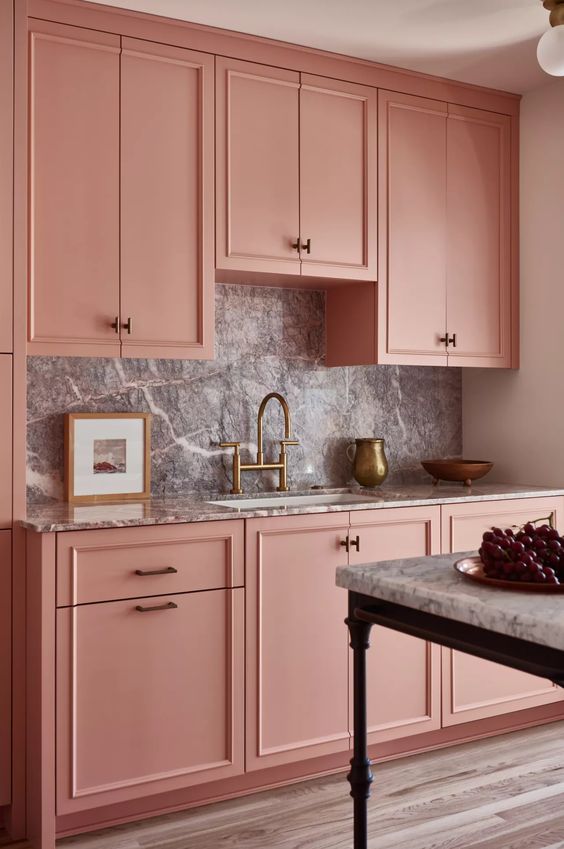A chic pink kitchen with a gray stone backsplash and countertop, brass and gold accents, and black is pure elegance