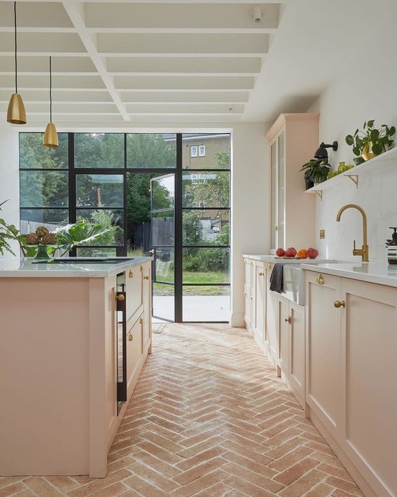 a delicate and chic blush kitchen with lower shaker cabinets, a kitchen island, white stone countertops and gold pendant lamps