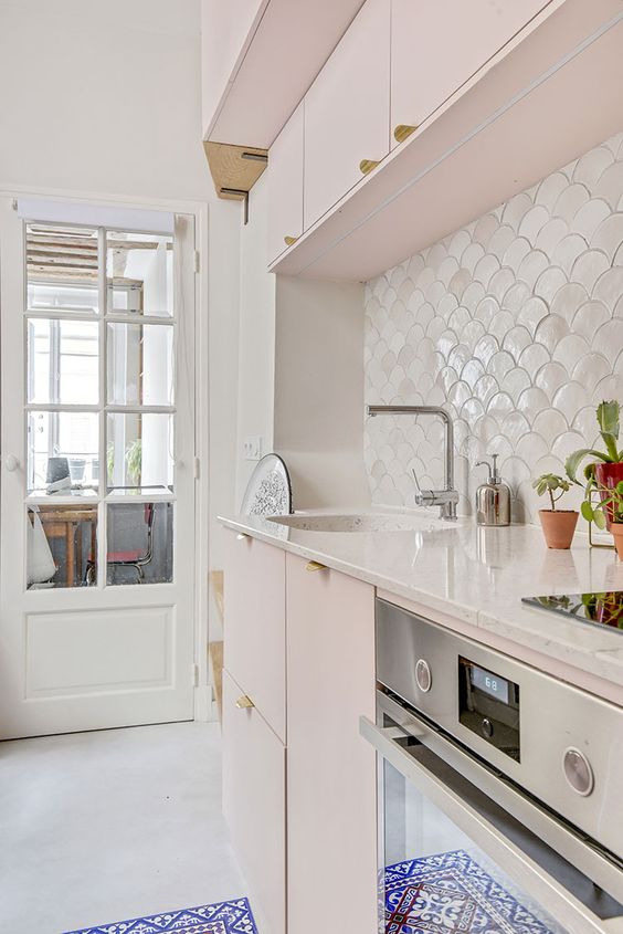 a soft blush kitchen with a white shell tile backsplash, white stone countertops and potted plants