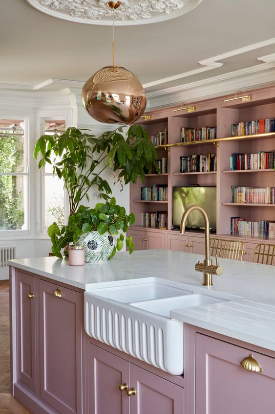 A purple kitchen with shaker cabinets, bookcases, a large island, and brass and gold accents is pure chic