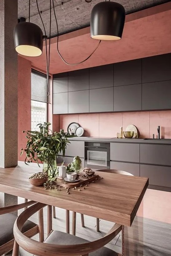 a minimalist pink kitchen with sleek graphite gray cabinets, a concrete ceiling and a small dining area