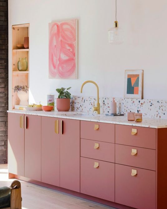 A modern and stylish pink kitchen with a terrazzo backsplash and worktops, gold fittings and a tap and a niche for storage