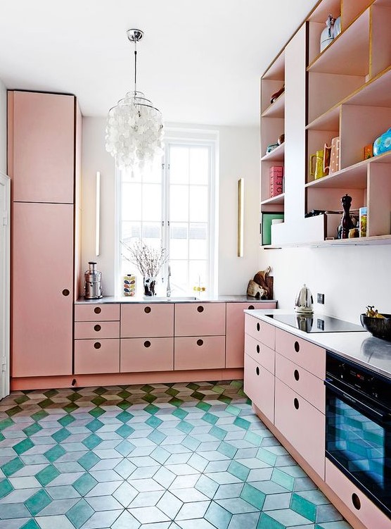 A modern pink kitchen with elegant cabinets, a statement chandelier and a green tile floor is very bold