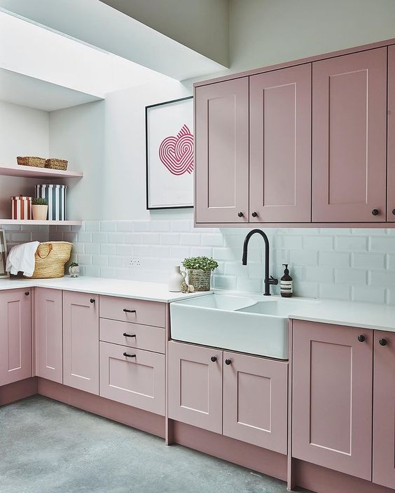 a pale pink kitchen with shaker-style cabinets, a white subway tile backsplash and white countertops, open shelving and a skylight