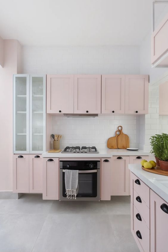 A pale pink kitchen with shaker cabinets, white stone countertops and a tiled backsplash and black handles is fantastic