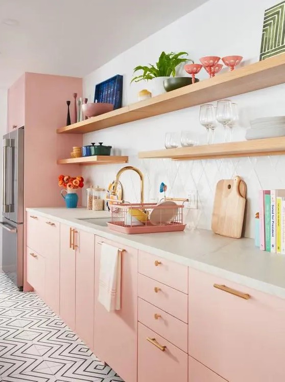 A pastel pink kitchen with plywood cabinets, white stone countertops, a white tile backsplash and gold handles