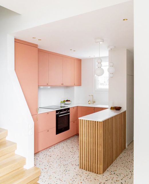 a peach-colored kitchen with a ridged island, white backsplash and countertops, and white pendant lamps