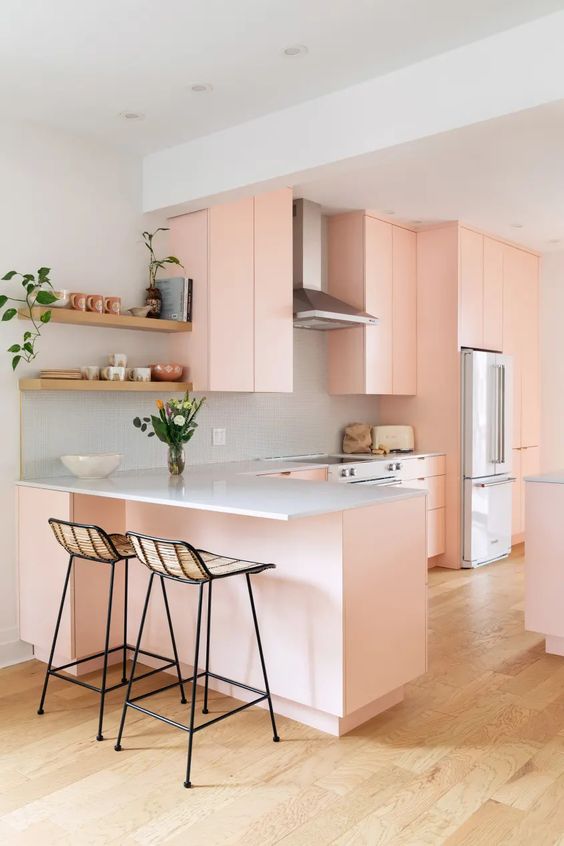 a peach-colored kitchen with sleek cabinets, a gray backsplash and countertops, flowers and greenery, and high stools