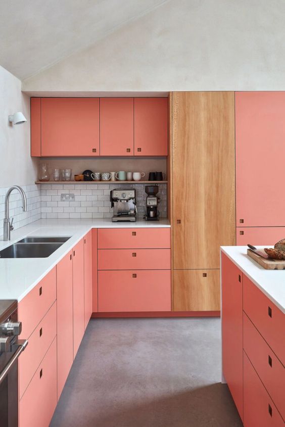 a pink kitchen with a white subway tile backsplash, a stained cabinet with no handles, and a shelf for storing decor